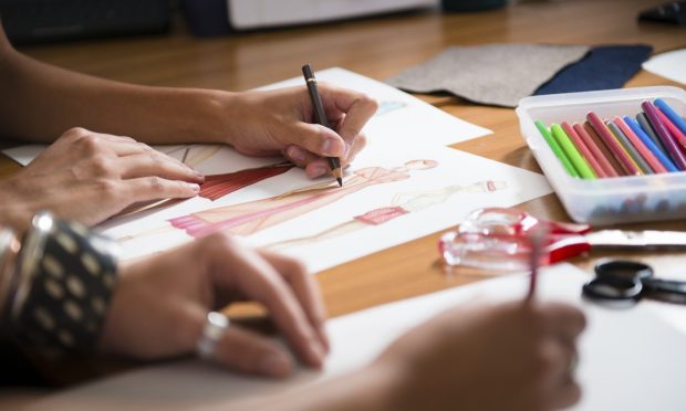 Two young women working as fashion designers and drawing sketches for clothes.