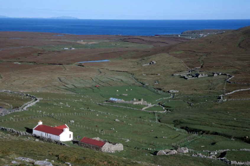 An isolated house amid fields on Foula with the sea in the distance 