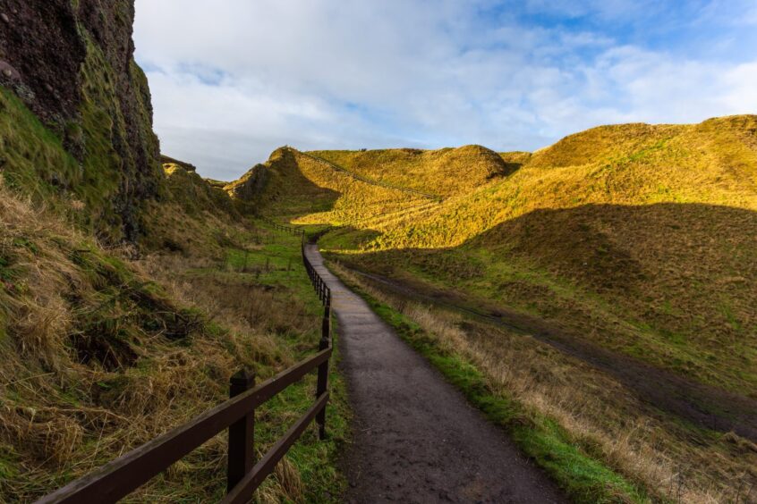 View of the path to the Dunnottar Castle between green hills, Stonehaven.