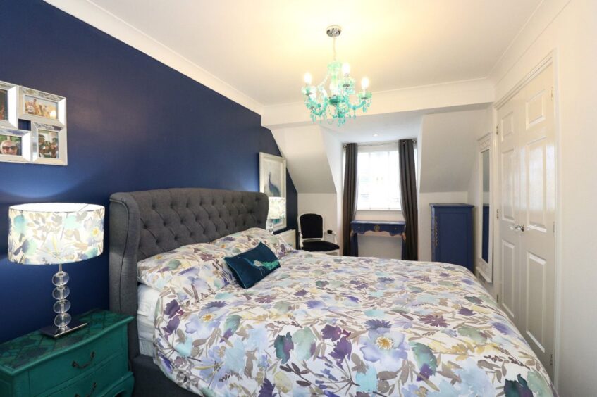 A bedroom with a double bed, navy blue accent wall, navy dresser and chest of drawers and floral accents