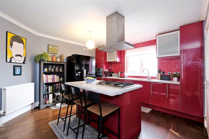Bright kitchen inside the Newburgh house for sale, featuring red kitchen cupboards, backsplash and island.