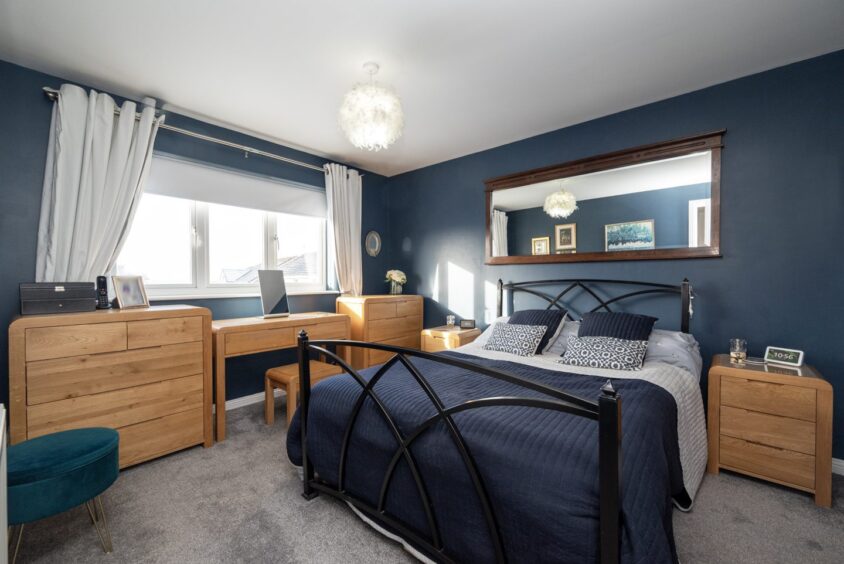 A bedroom in the renovated Oldmeldrum home with navy blue walls and bedding and wooden dressers