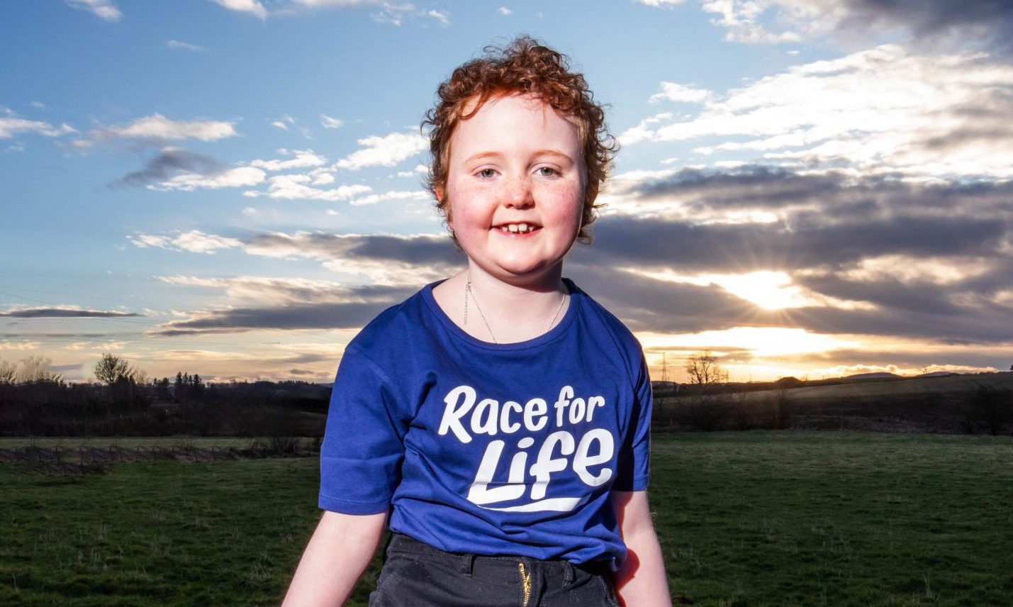 Aurora Farren siting on a fence wearning a blue Race for Life T-shirt.
