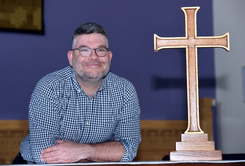 The Rev Scott Rennie smiling next to a wooden cross