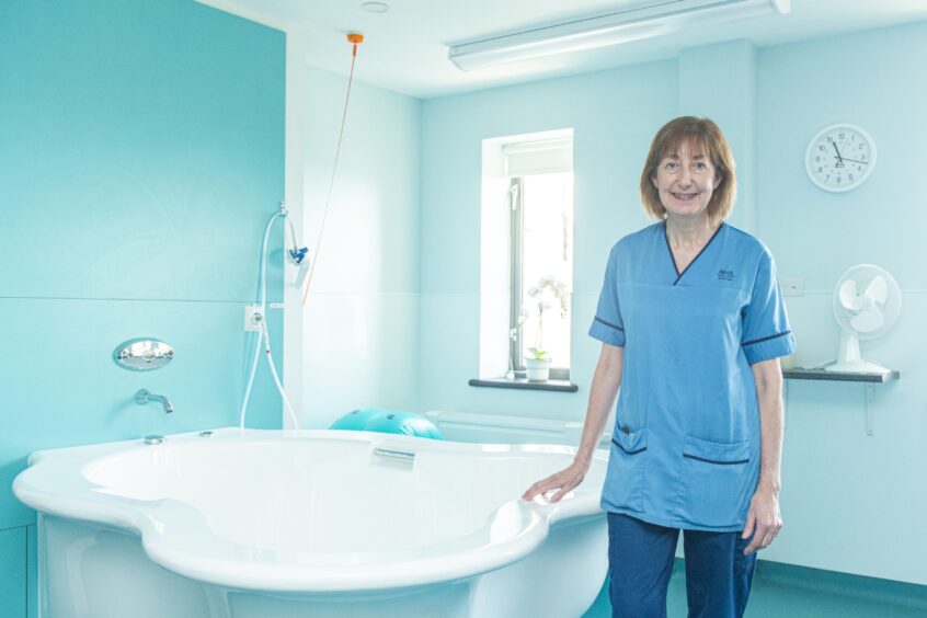 Nairn midwife Maggie Macleod wears nursing scrubs and stands next to a water birth pool in Dr Gray's