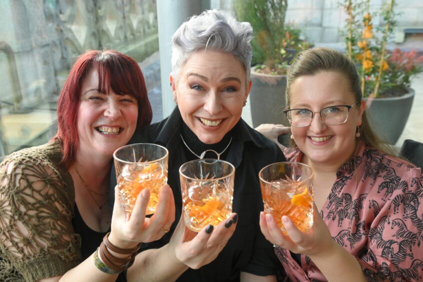 Three women smiling with their cocktails. 