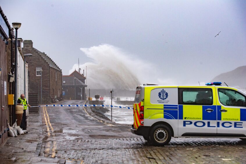 police van sits next to a cordon at Stonehaven Harbour as waves crash into the pier.