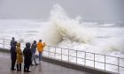 Waves lash against Aberdeen seafront as spectators look on.