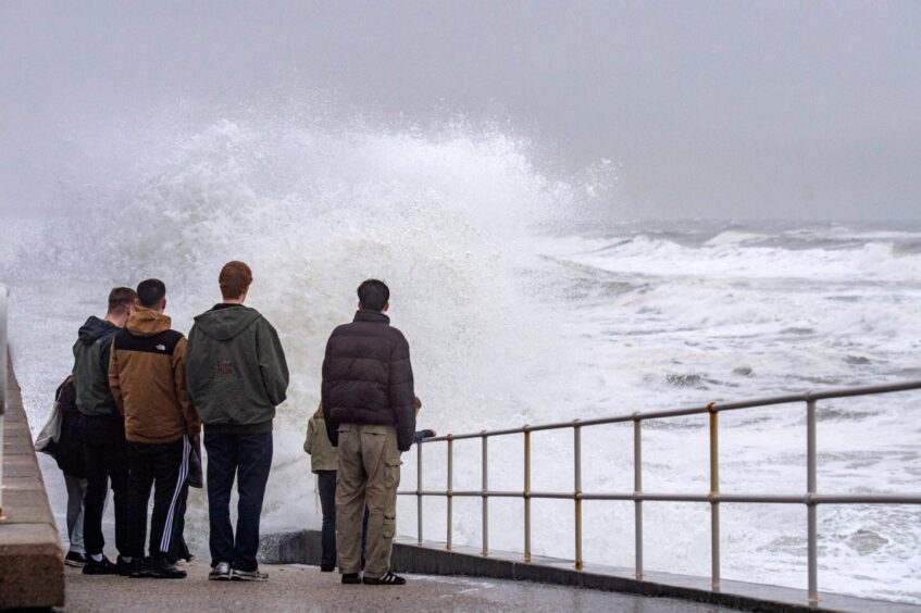 Spectators watch as the waves hit the seafront creating a large amount of spray.