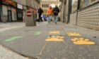 Yellow paw prints and green footprints painted on a pavement