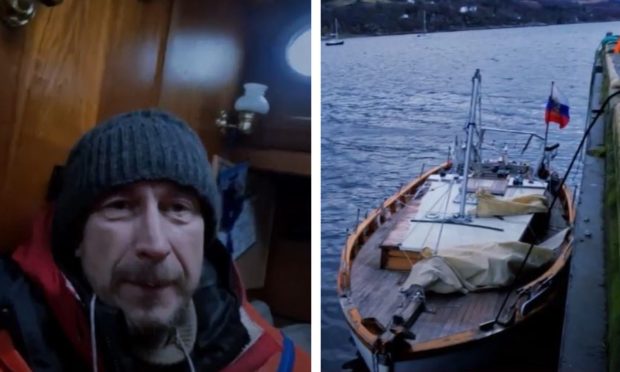 Roman Titov pictured onboard his yacht wearing a red rain coat and a blue hat.