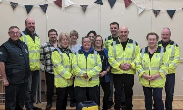 People wearing paramedic uniforms stand smiling in front of bunting.