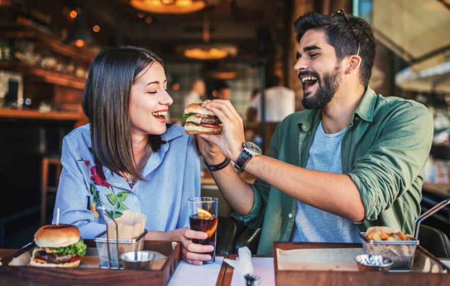 Shutterstock image two people eating burgers and smiling in a restaurant. 