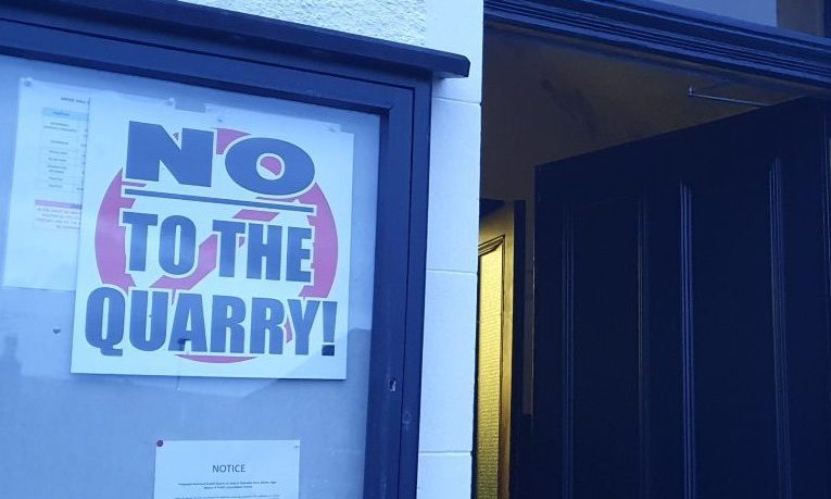 Entrance to Birnie Hall with "no to the quarry" sign outside.