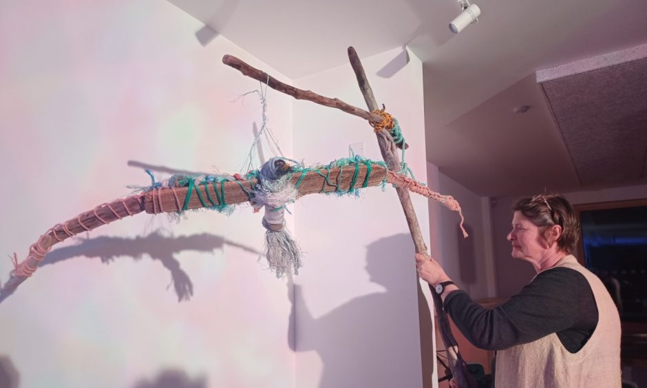A woman holds up a sculpture of an albatross with its wings outstretched, made of wood and plastic.