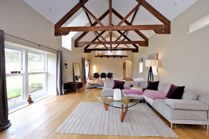 The lounge in the Aberdeenshire steading conversion featuring Douglas fir beams, overlooked from a galleried area.