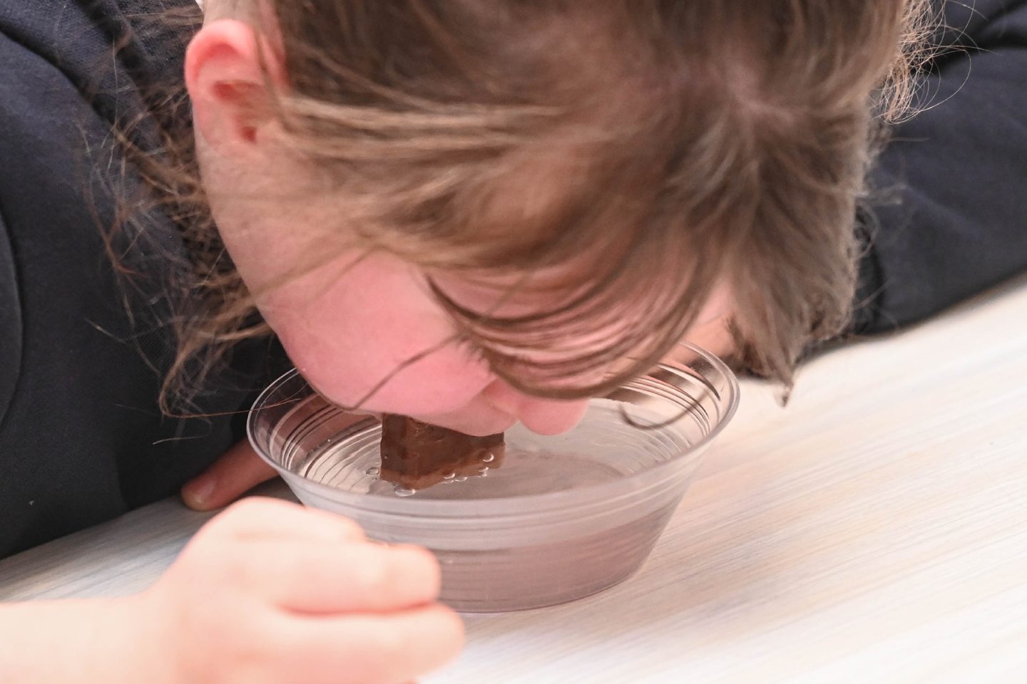 A child dipping a bar of chocolate in a bowl with their mouth