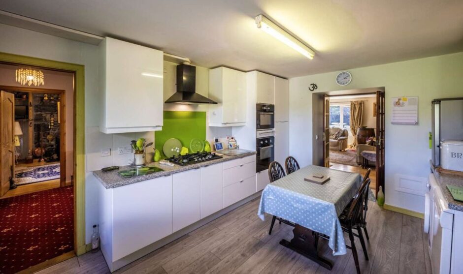 Modern white kitchen worktops with a green splash back wall and a dining table in the middle