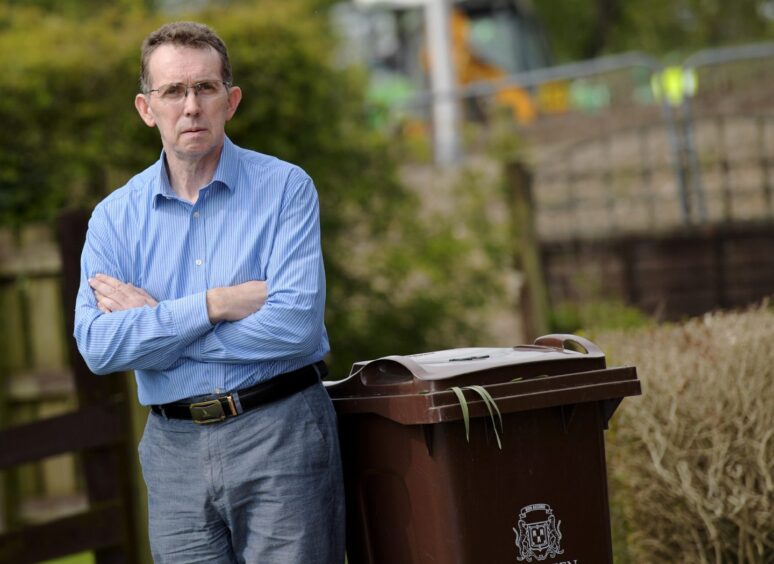 Councillor Steve Delaney standing beside a brown garden waste bin.