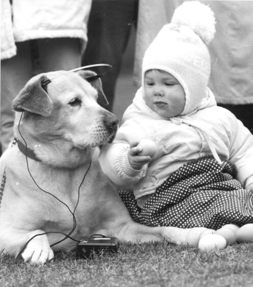 A baby holding an egg with a dog next to her with a walkman