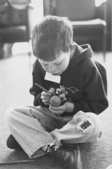 A boy sitting cross-legged painting an egg for easter in the north-east of scotland