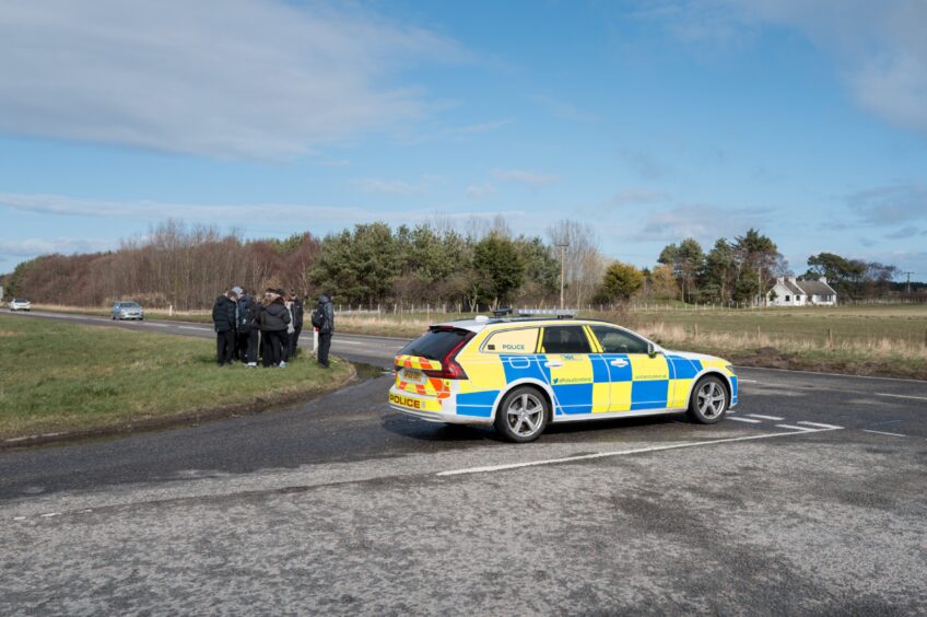 Teenagers leave tributes at roadside in front of police car.