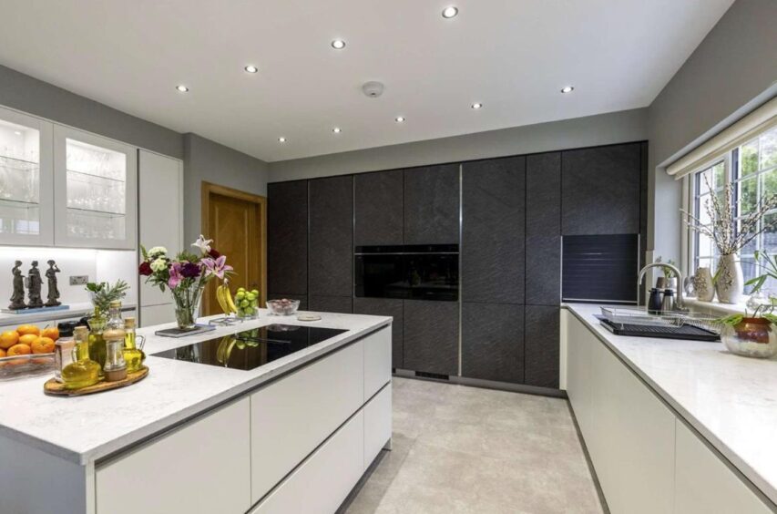 The kitchen, which has grey floor tiles, white cupboards with marble countertops and the back wall has wall length black cupboards