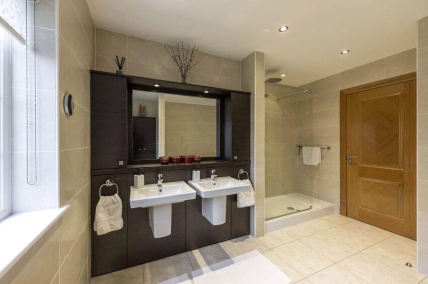 The bathroom's cubicle shower and two sinks with a large mirror above them with two cabinets on either side