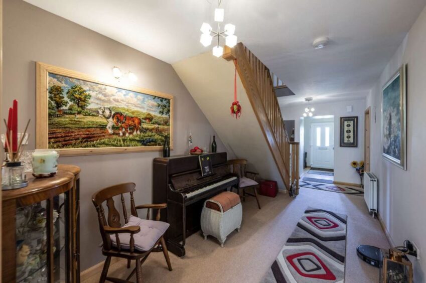 A long hallway with a piano under the stairs and a rug running up the main drag.