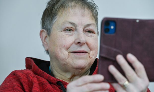 Bev Dyson holding mobile phone up looking at camera.