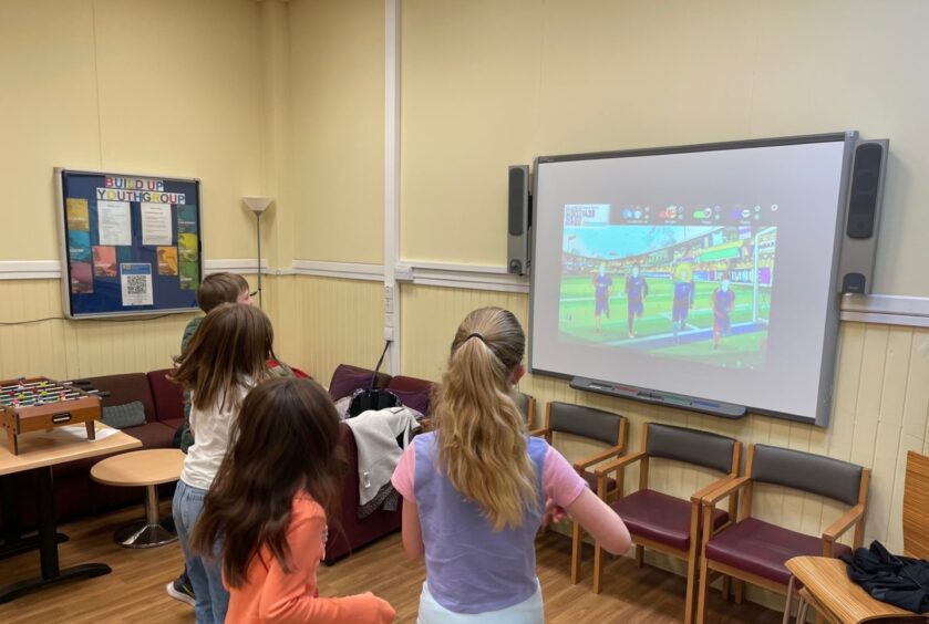 Four children playing a motion capture video game projected on a screen in a hall