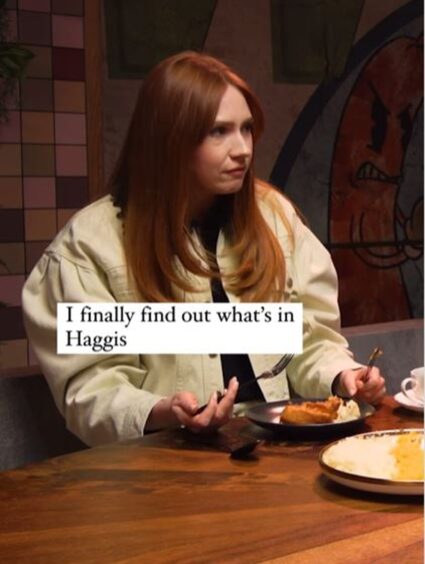 Karen Gillan pictured with ginger hair and wearing a cream jacket eating a plate of Haggis, turnip and potatoes.