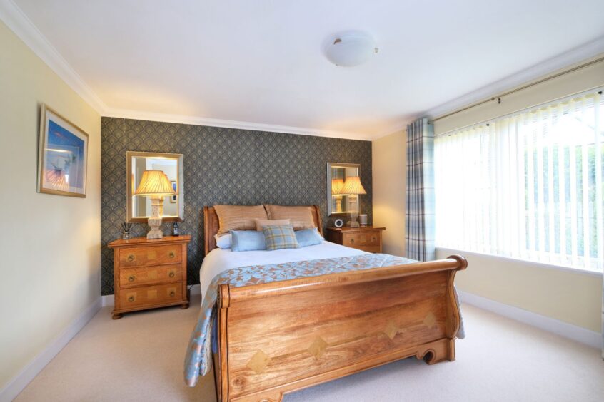 The cosy bedroom in the Maryculter home with a double bed, two chest of drawers and a papered accent wall