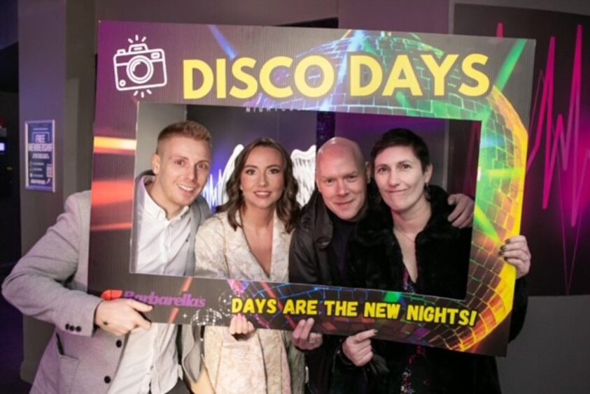 Four people holding up a carboard frame that reads 'Disco Days: Days are the new nights!'