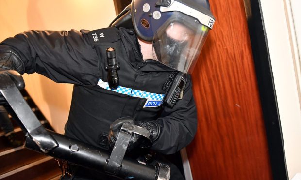 Policeman carries batton preparing to knock down a door in the Headland Court area, Aberdeen.