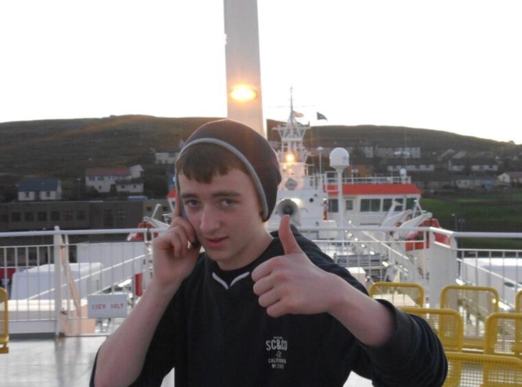 Aiden gives a thumbs up to camera while standing on a boat and talking on the phone