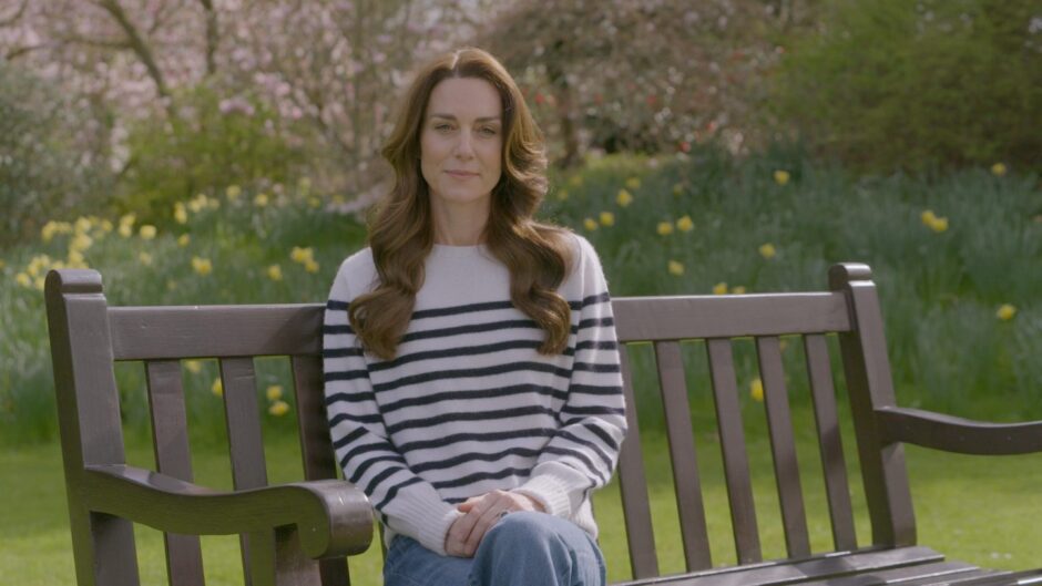 Kate, the Duchess of Wales sitting on a bench in the garden wearing a while and blue striped jumper.