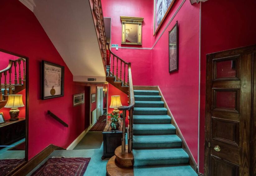 One of two staircases in the home, with deep red walls and green carpet.