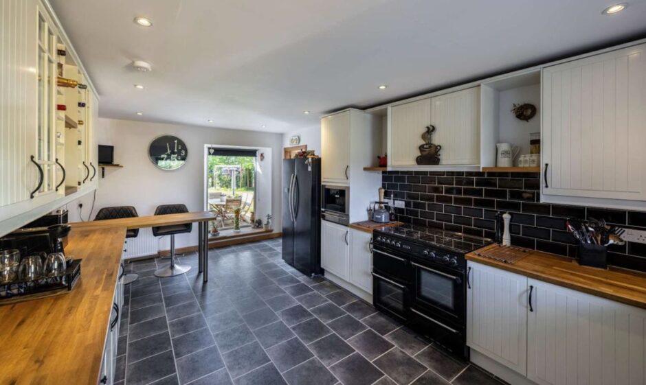 Modern Kitchen with black tiled flooring, black coocker and while cupboards with wooden worktops. 