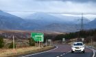 White car drives on the A9 Inverness to Perth road near Dalwhinnie with the hills in the background.