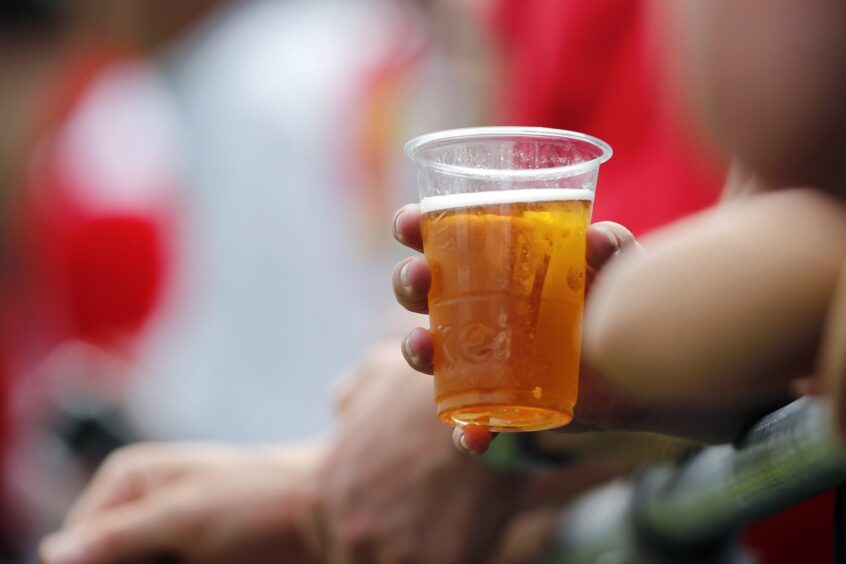 Pictured is a pint of beer being held by a fan at a football match.