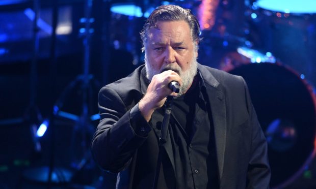 Russell Crowe sings into the microphone as he performs on stage with the Gentlemen Barbers