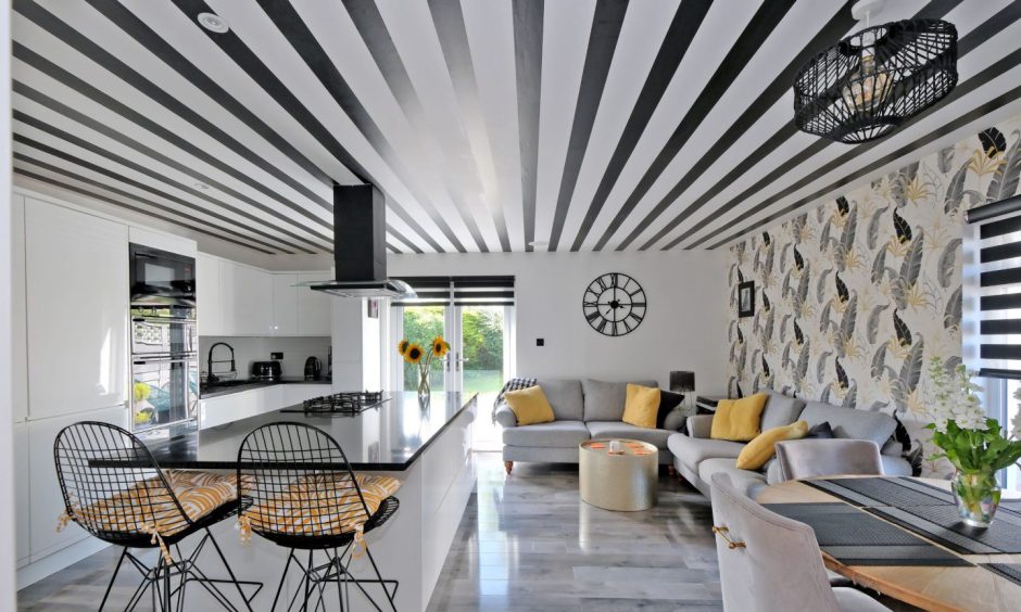 The open plan kitchen, dining and living room with a leaf-print accent wall, black and white striped ceiling, and black, white and yellow colour scheme