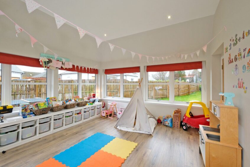 The sun room which is being used as a colourful playroom for children. There are number decals on the walls, toys in organised bins and bunting hung from wall-to-wall