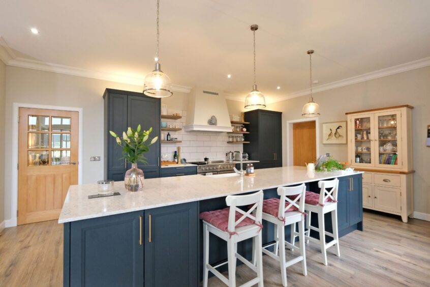 The kitchen with navy cupboards and white marble countertops. The kitchen island has three white bar stools