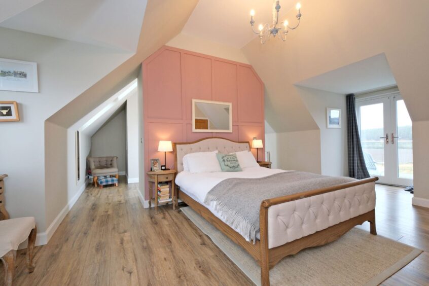One of the bedrooms in the Royal Deeside home with a panelled pink accent wall behind the double bed and double glass doors leading out to the balcony