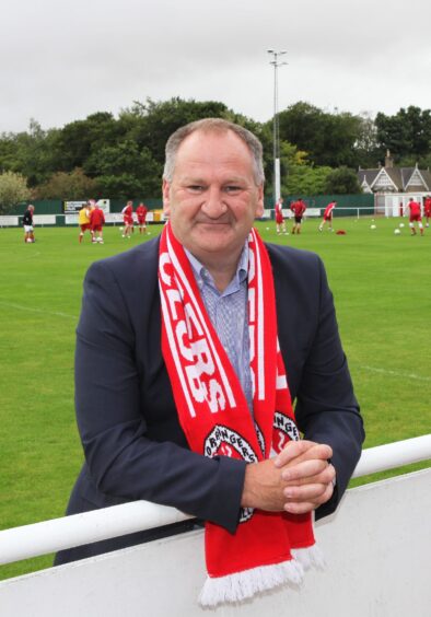 Brora Rangers' benefactor Ben Mackay on the side of the pitch with a scarf on