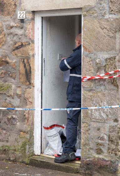 Police officer with evidence bag at fire-hit Forres property.