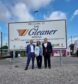 Scott, Jane and son Evan standing in front of sign for Gleaner arena.