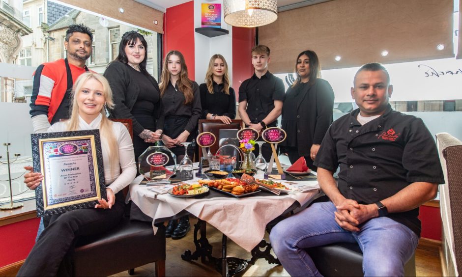 Staff of Panache restaurant in Elgin, sitting at table with Indian food and awards.